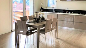 Een moderne keuken met een groot raam, een eethoek met een tafel en stoelen, en uitzicht op een gebouw met rode dakpannen.