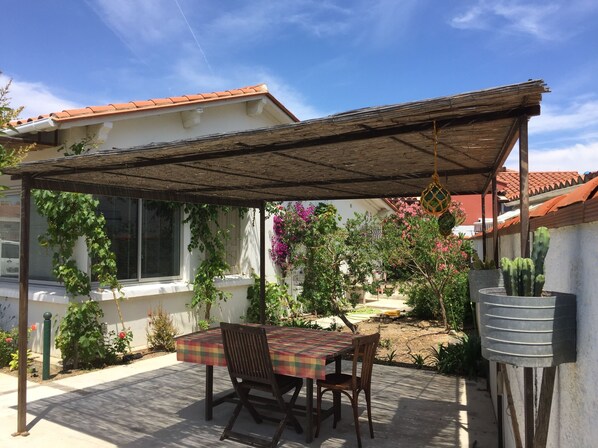 A covered patio with a table and chairs, surrounded by potted plants and a cactus.
