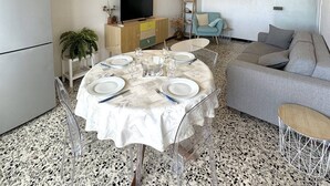A modern living room with a grey sofa, a dining table set for four, and a flat-screen TV on a wooden cabinet. - Very nice apartment with sea view and private parking 4SUF502 (LE BARCARES)