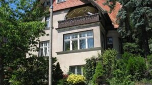A two-story house with a red-tiled roof, large windows, and a brick entrance.