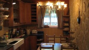 A compact kitchen with wooden cabinets, a dining table with chairs, and a window with curtains.