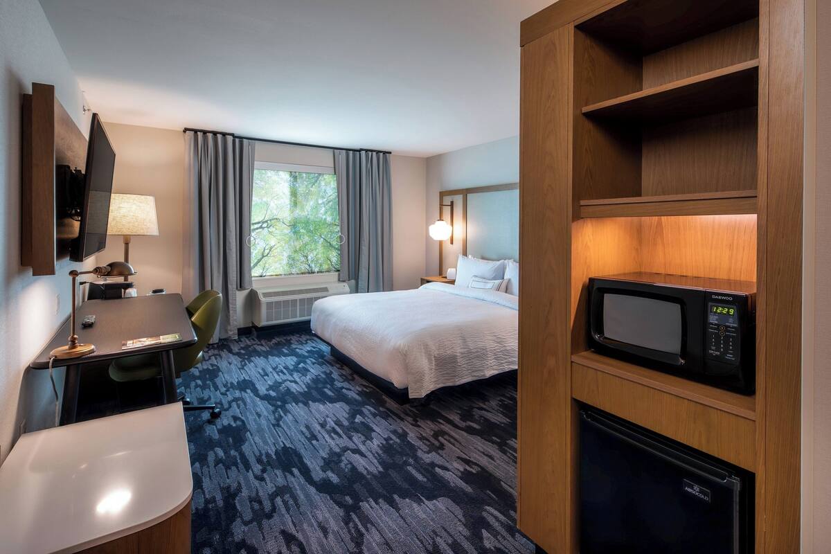 Habitación de hotel con cama, escritorio, silla, televisión, microondas y refrigerador.