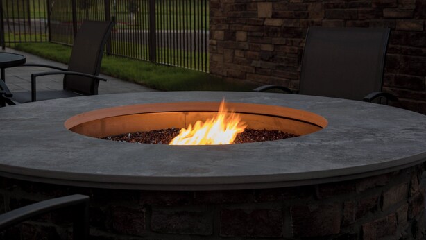 A circular stone fire pit with a fire burning inside, surrounded by chairs and a stone wall. - Fairfield Inn & Suites by Marriott Little Rock Airport (Little Rock)