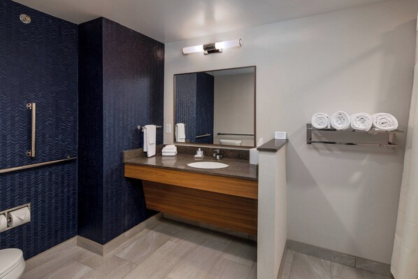 A modern bathroom with a dark patterned wall, a wooden vanity, a large mirror, and a shelf with rolled towels.