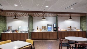 A modern cafe with wooden furniture, a counter with various food items, and a seating area with tables and chairs. - Fairfield Inn & Suites by Marriott Little Rock Airport (Little Rock)