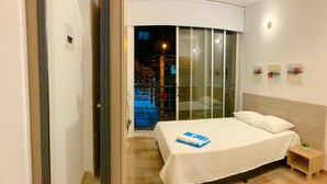 A modern hotel room with a large bed, a small bedside table, and a view through a sliding glass door to an outdoor area. - Laureles Apartments! (Medellín)
