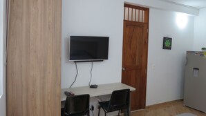A small room with a wooden door, a TV mounted on the wall, a table with two chairs, and a refrigerator. - Laureles Apartments! (Medellín)