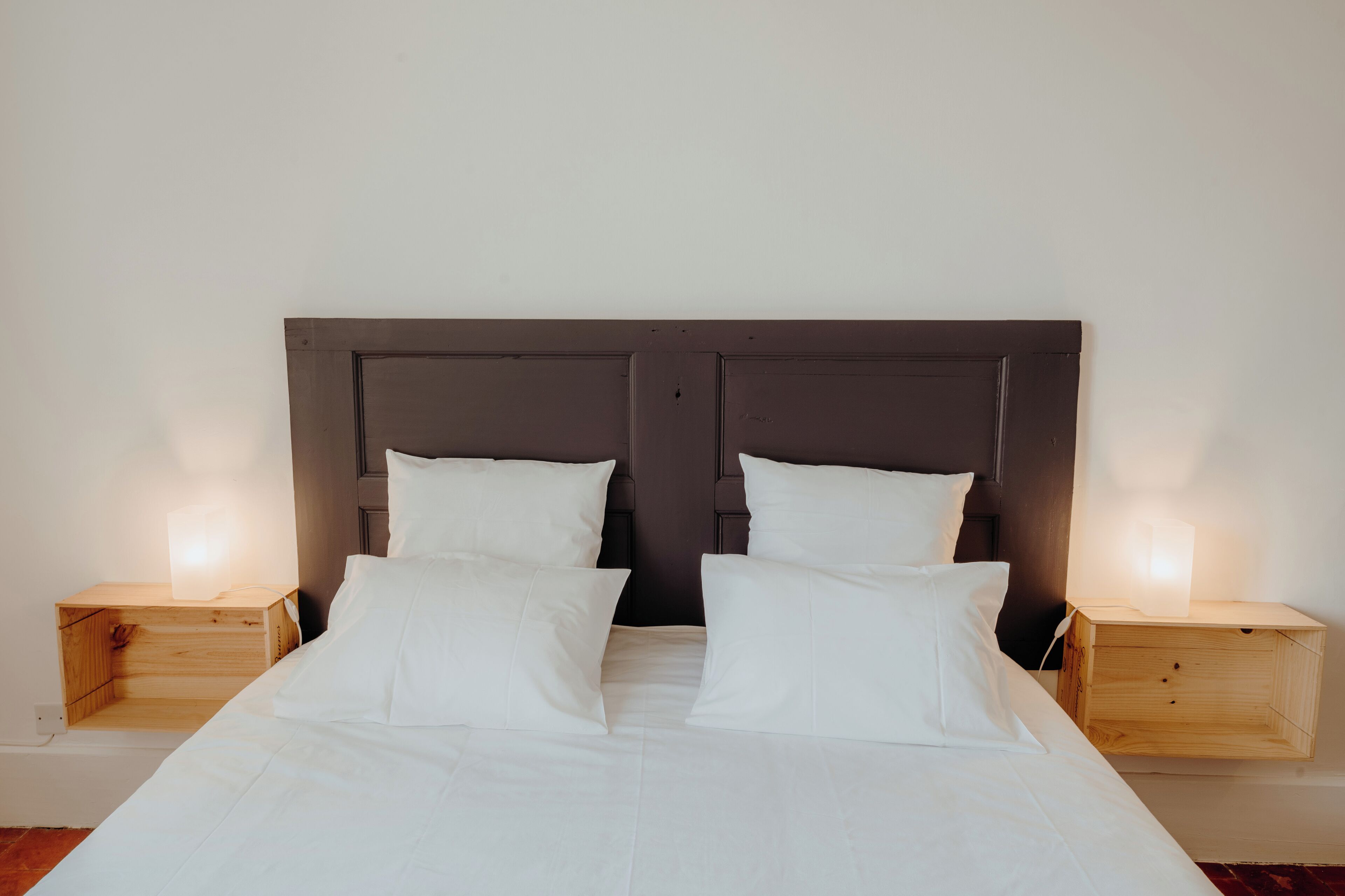 Un lit double avec une tête de lit en bois, deux tables de chevet avec des lampes et du linge de lit blanc.