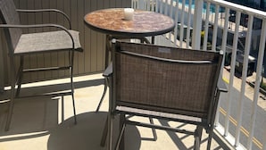 Un balcón con una mesa redonda y dos sillas, con vistas a una playa y un edificio de varios pisos.
