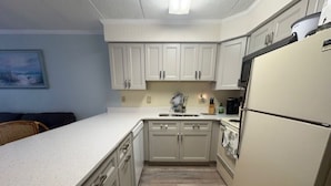 Cocina compacta con armarios blancos, una encimera, un fregadero y un refrigerador.