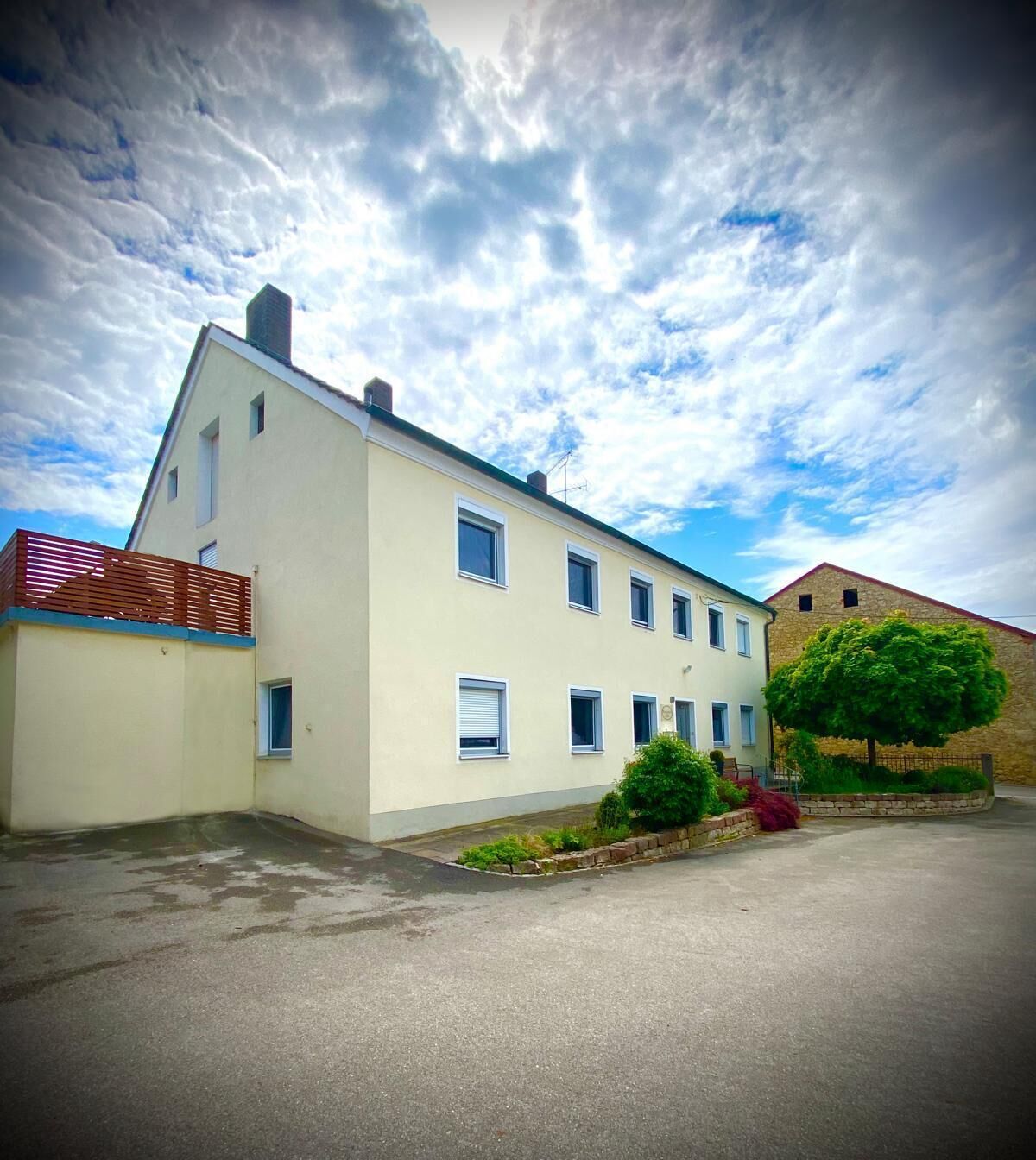 A two-story building with a flat roof, a small balcony, and a paved driveway.
