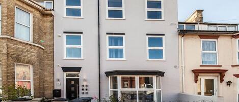 A multi-story residential building with a flat facade, large windows, and a small front porch area.