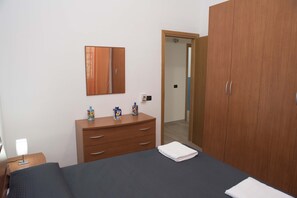 A bedroom with a bed, a wooden dresser, a mirror, and a door leading to another room. - Villa Eden Luxore (SCIACCA)