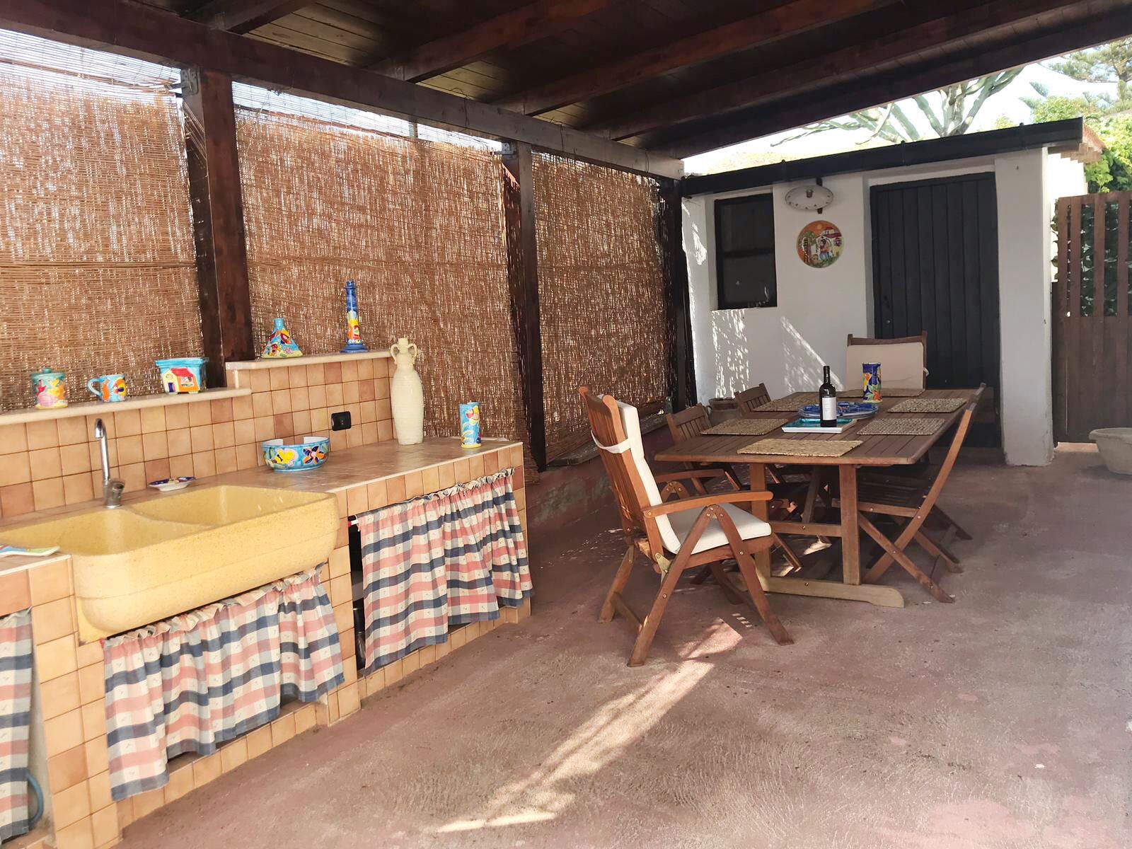 An outdoor kitchen with a sink, wooden table, chairs, and a decorative wall.