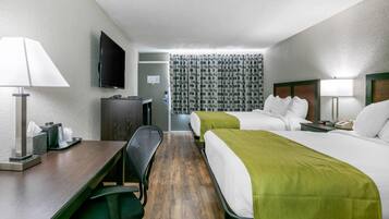 A hotel room with two beds, a desk, a chair, a TV, and a bathroom visible through a curtain.