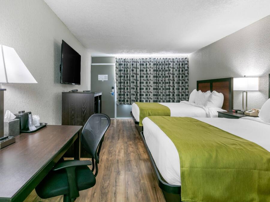 A hotel room with two beds, a desk, a chair, a TV, and a bathroom visible through a curtain.