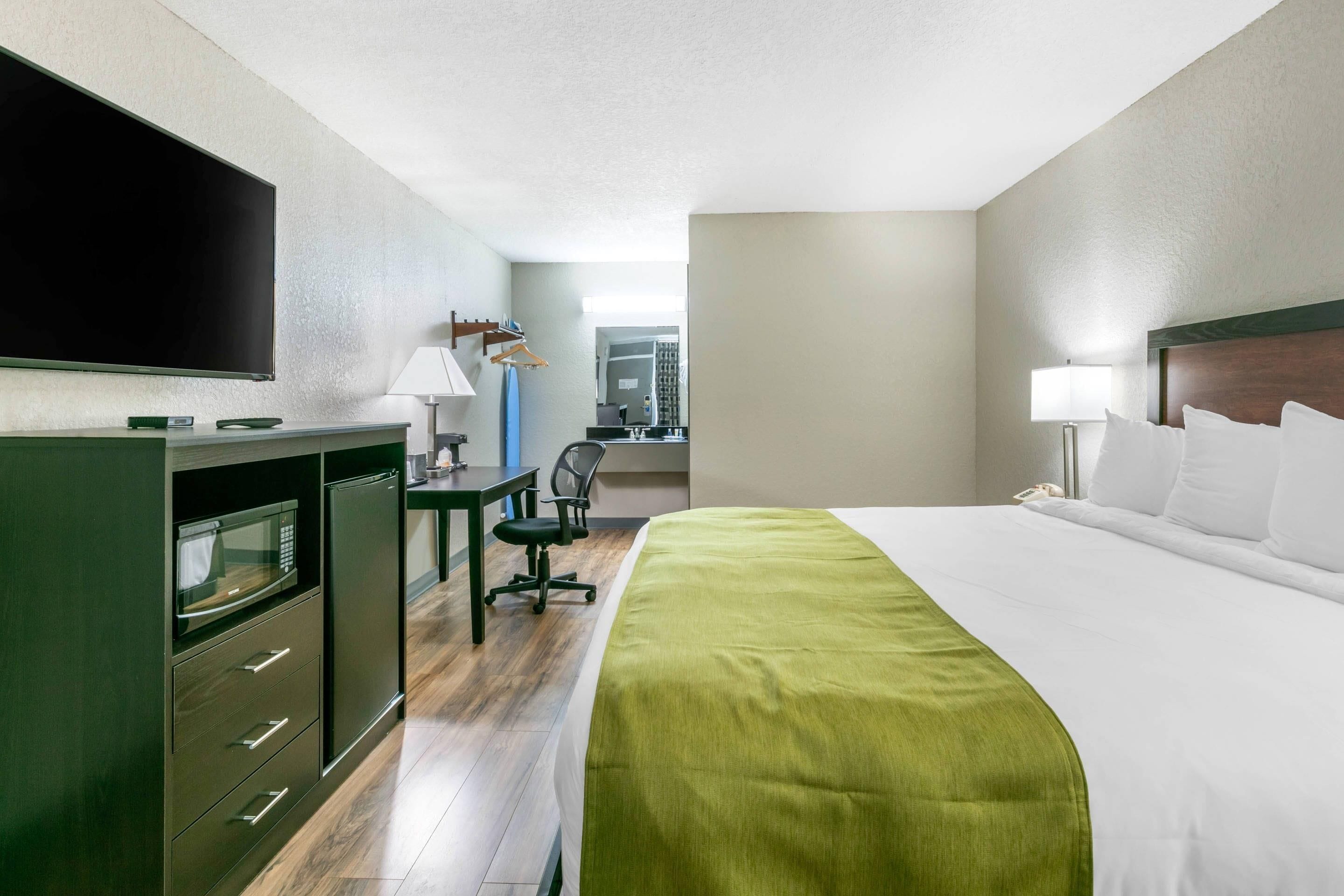 A hotel room with a bed, a desk, a television, and a view of the outside.