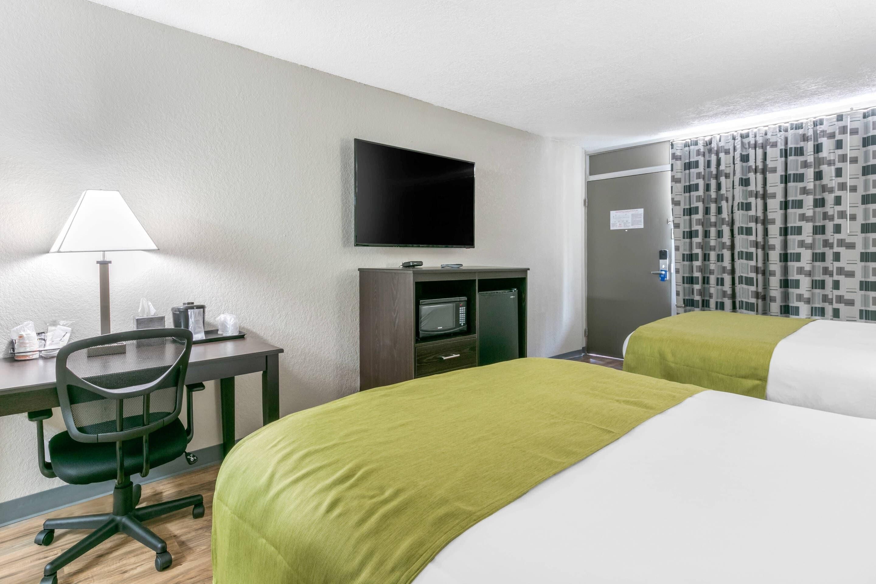 Quarto de hotel com escrivaninha, cadeira, televisão, micro-ondas e duas camas.