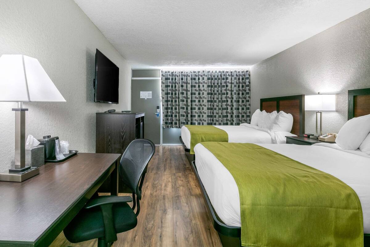 A hotel room with two beds, a desk, a chair, a television, and a bathroom visible through a curtain.