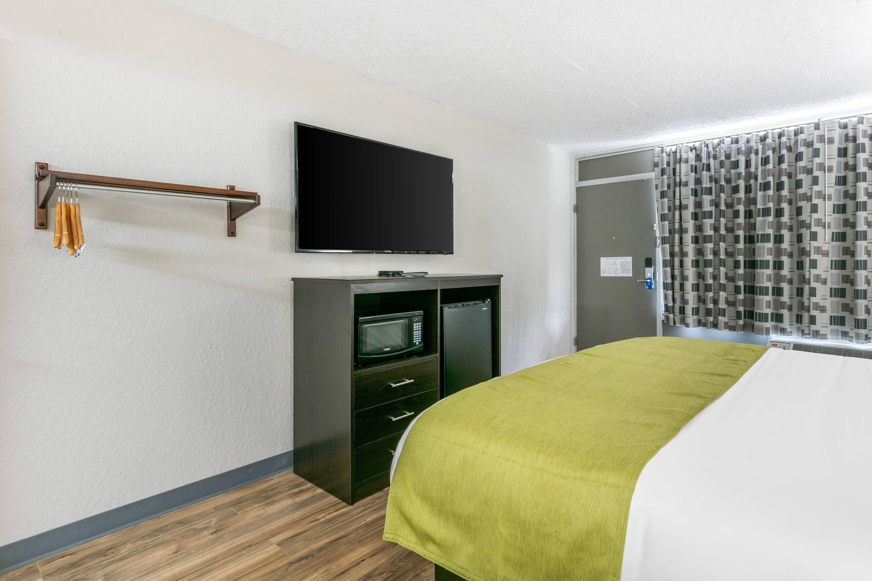 A hotel room with a bed, a flat-screen TV mounted on the wall, a microwave, and a small refrigerator.