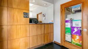 A reception area with a wooden reception desk, a check-out time sign, a notice about photo ID, and a door with wine boxes.