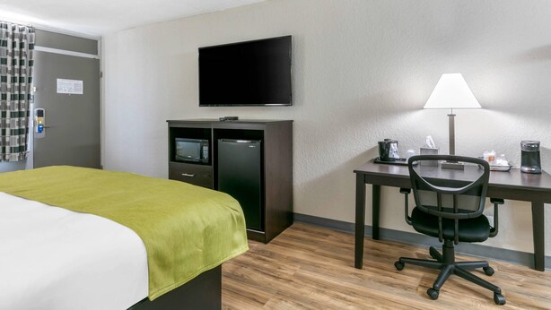 A hotel room with a bed, a desk with a chair, a flat-screen TV, a microwave, a refrigerator, and a coffee maker.