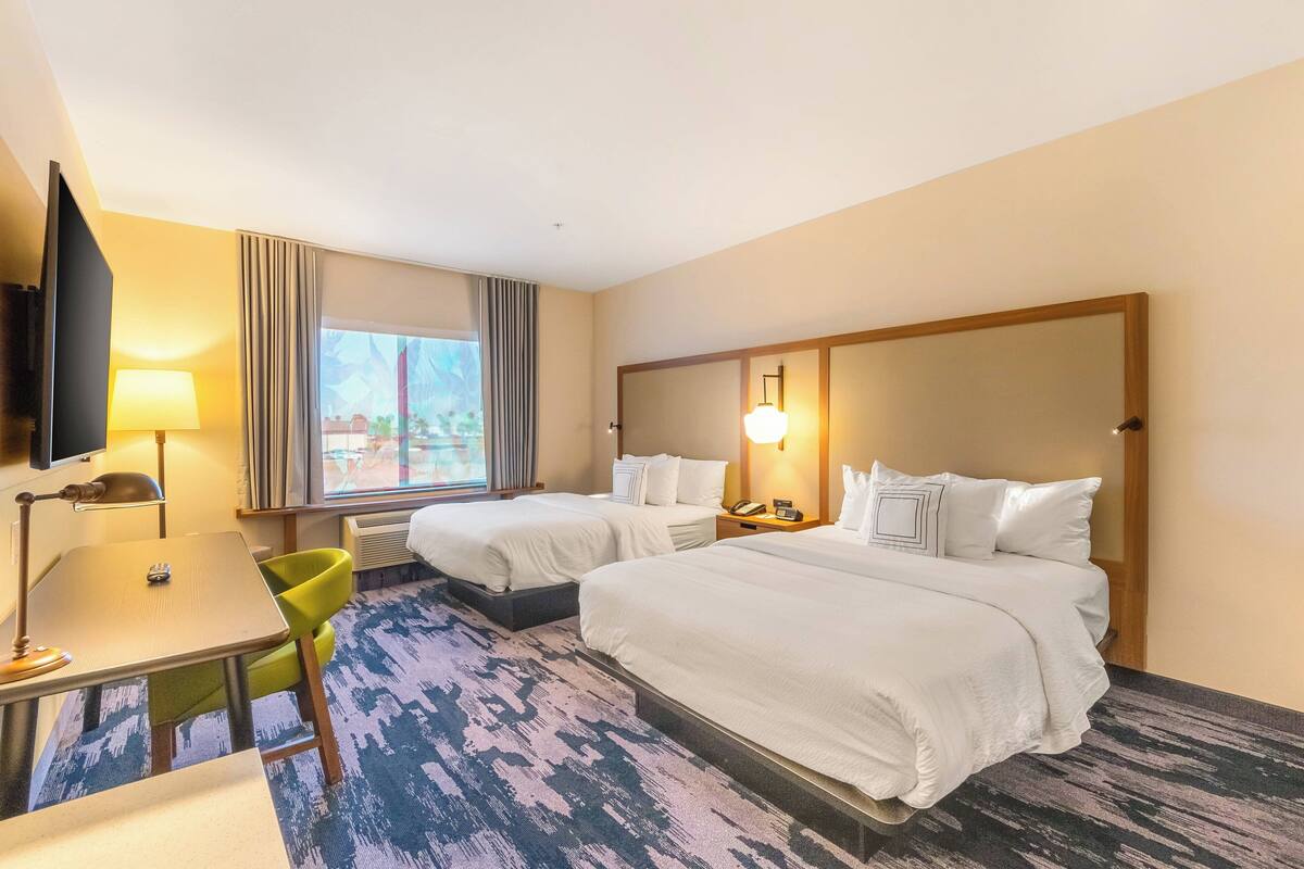 Une chambre d’hôtel avec deux lits, un bureau, une chaise, une télévision et une fenêtre avec des rideaux.