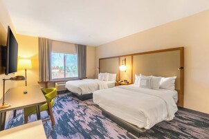 A hotel room with two beds, a desk, a chair, a TV, and a window with curtains.