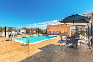 A swimming pool with a tiled deck, lounge chairs, and umbrellas.