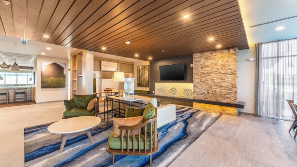 Un vaste espace de vie doté d’un plafond en bois, d’un mur décoratif en pierre, d’un téléviseur à écran plat et d’un coin salon comprenant un canapé et un fauteuil.
