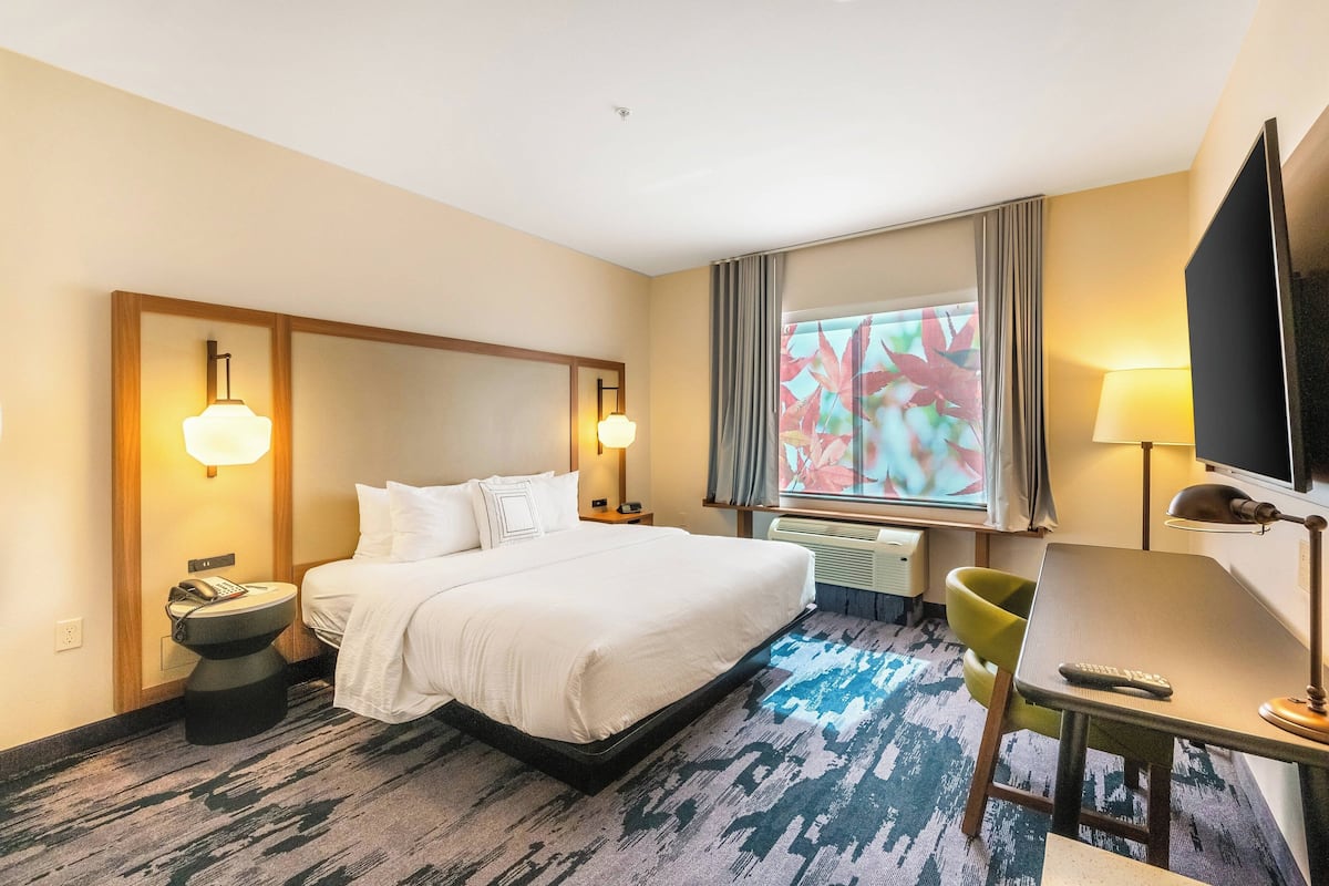 Une chambre d’hôtel avec un grand lit, des tables de chevet avec des lampes, un bureau avec une chaise, une télévision et une fenêtre avec des rideaux.