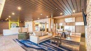 Un hall d’hôtel moderne avec un plafond en bois, un comptoir d’accueil, un canapé, un coin repas et un mur décoratif en pierre.