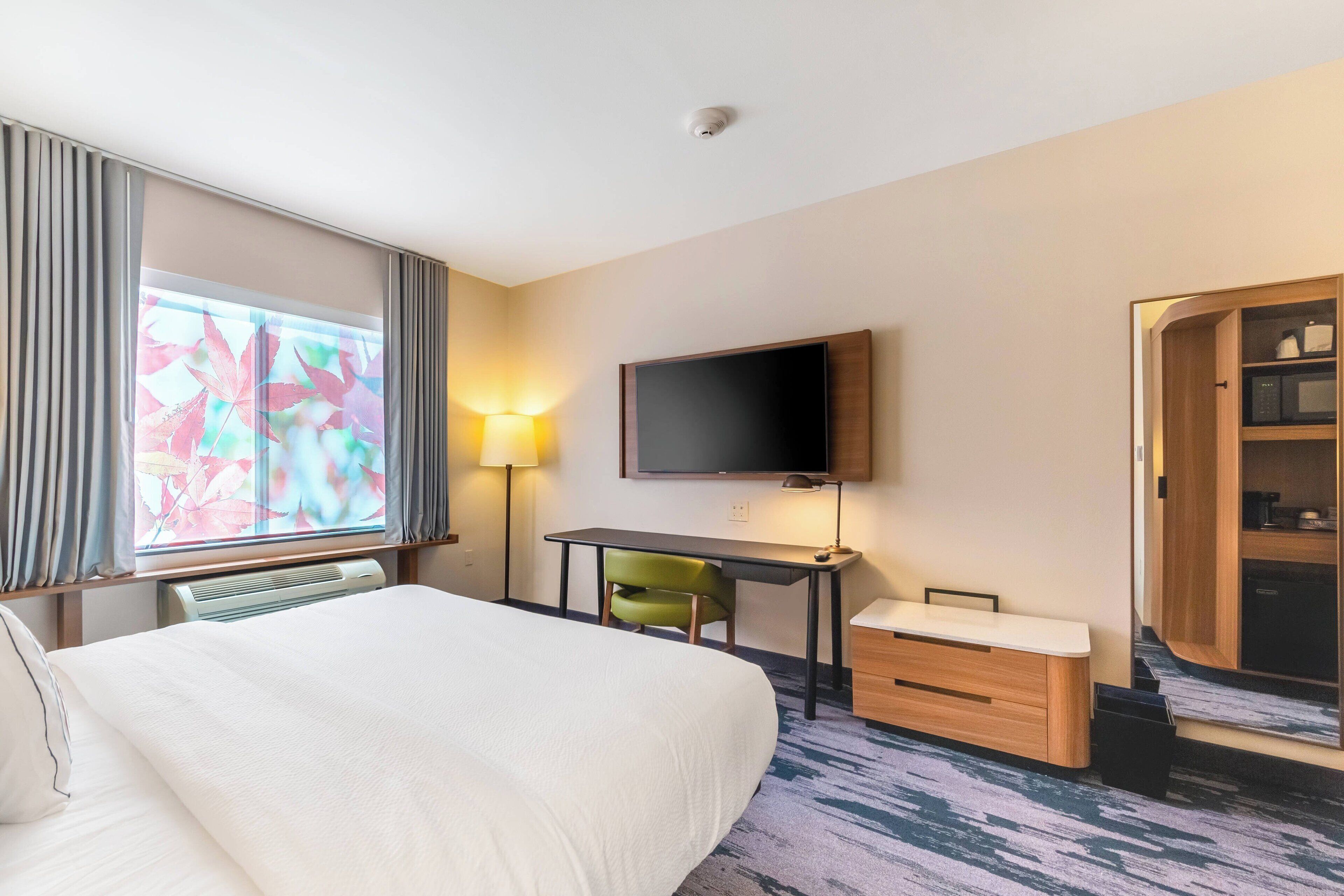 A hotel room with a bed, desk, chair, TV, and wardrobe.