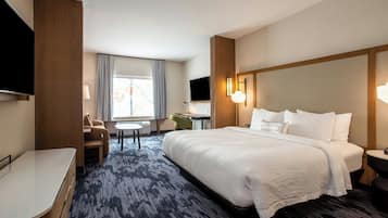 Une chambre d’hôtel avec un grand lit, un bureau, une chaise, une télévision et une fenêtre avec des rideaux.