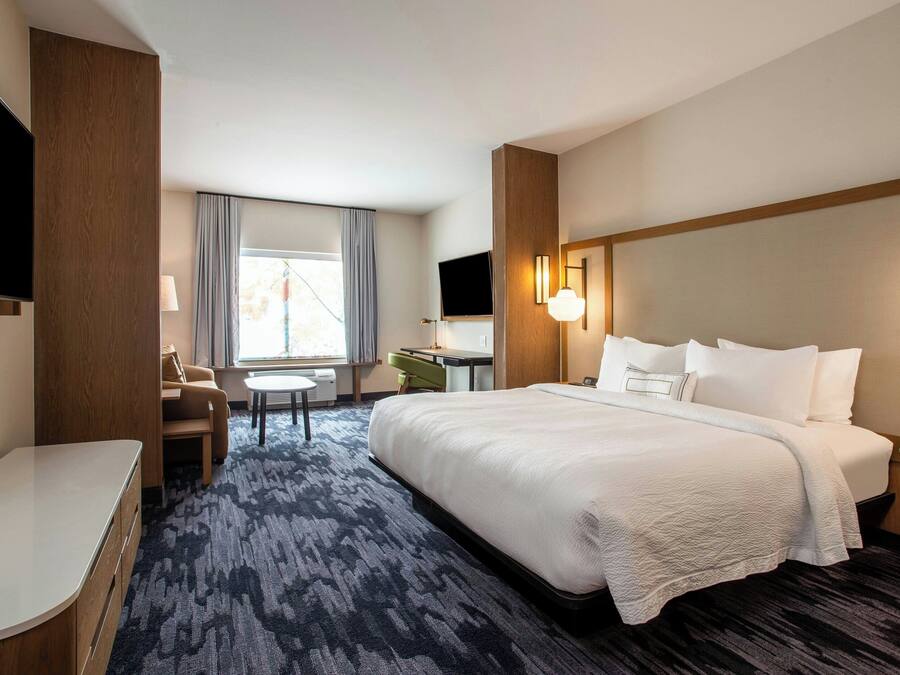 Une chambre d’hôtel avec un grand lit, un bureau, une chaise, une télévision et une fenêtre avec des rideaux.