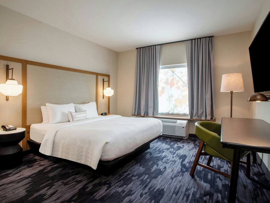 Een hotelkamer met een groot bed, een bureau, een stoel, een televisie en een raam met gordijnen.