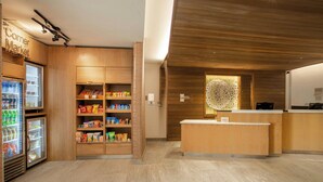 A reception area with a wooden reception desk, a refrigerator stocked with beverages, and shelves with snacks. - Fairfield Inn & Suites by Marriott Greenville Spartanburg/Duncan (Duncan)