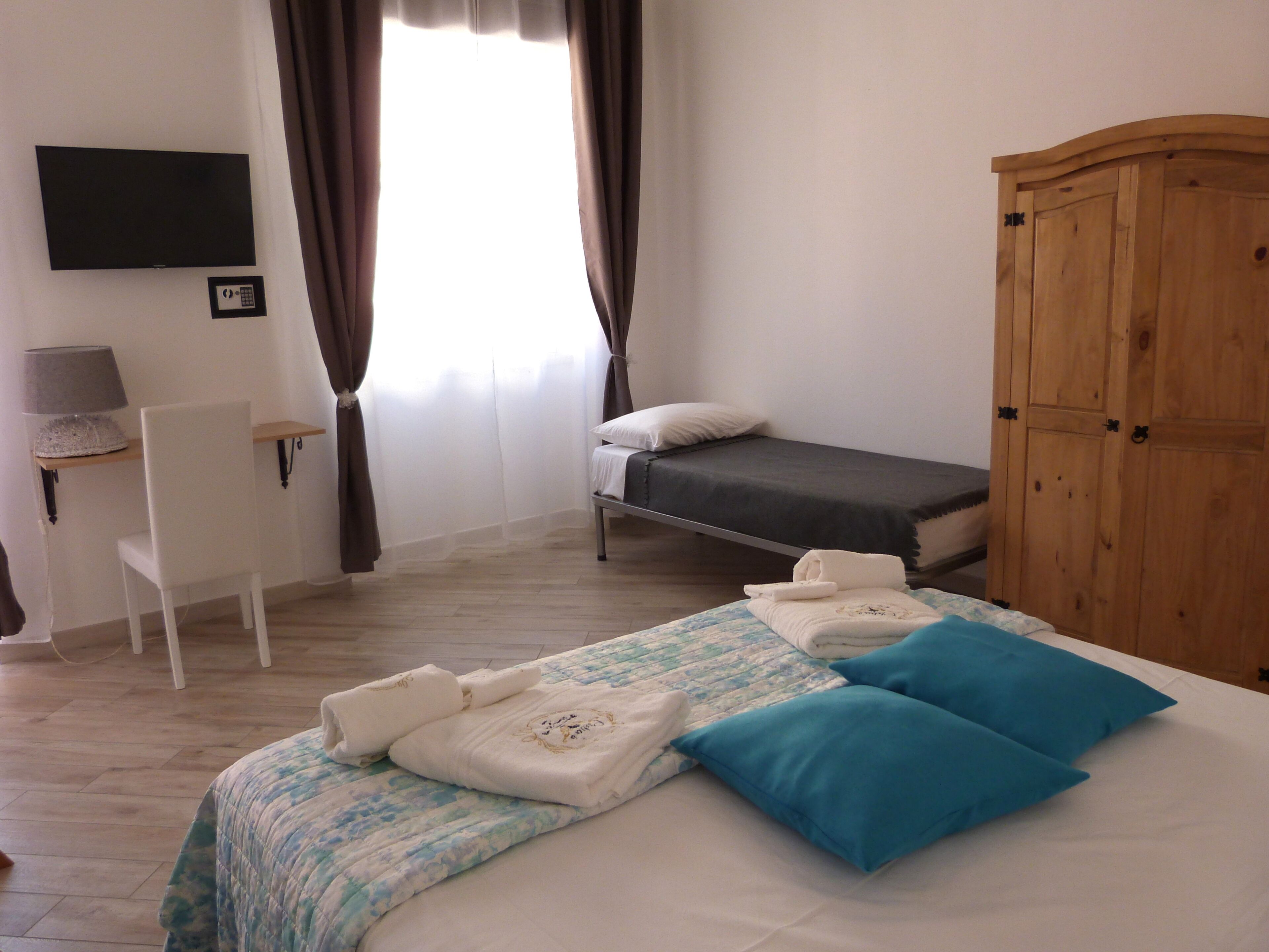 Ein Schlafzimmer mit Bett, Schreibtisch, Stuhl, Kleiderschrank und einem Fernseher an der Wand.