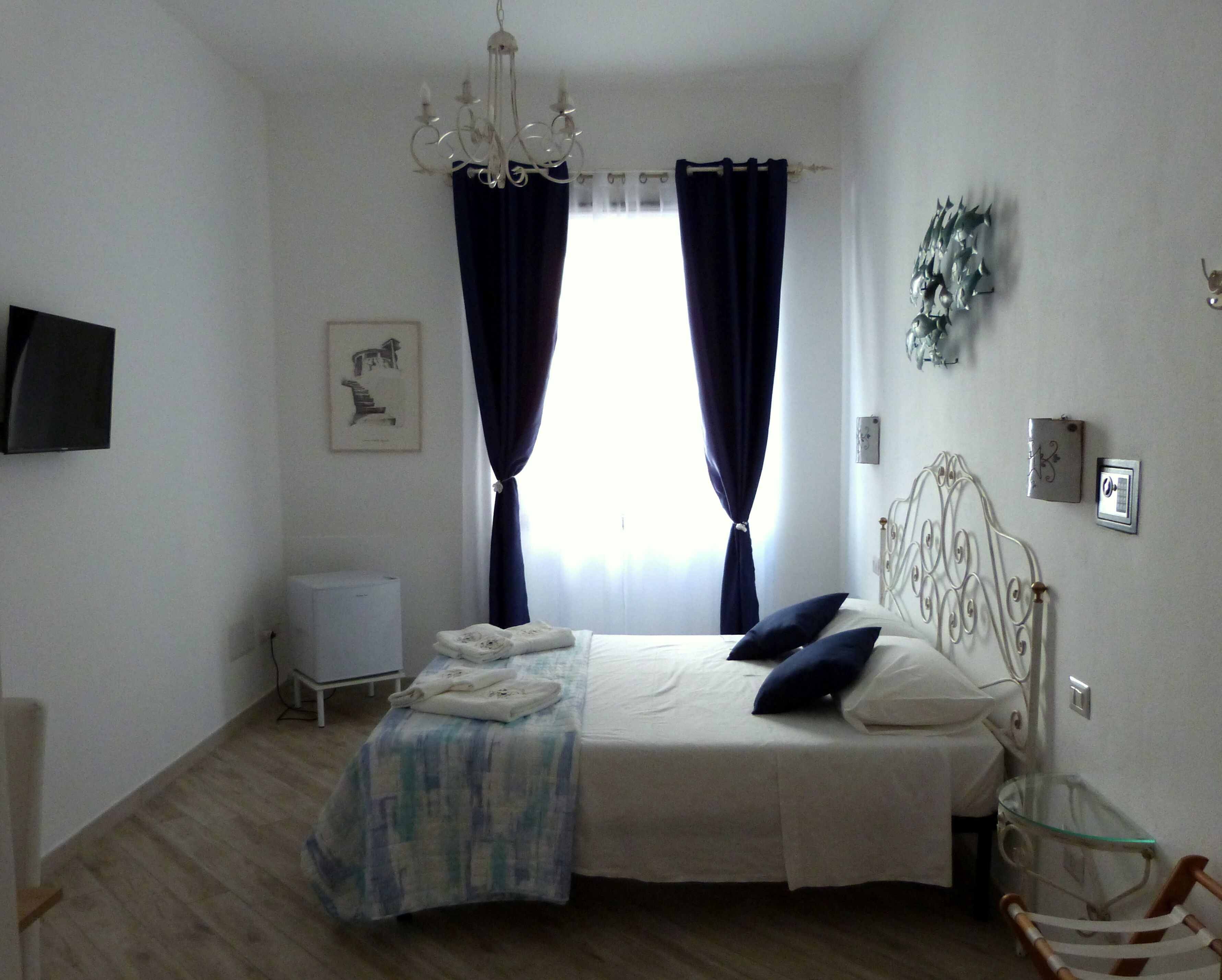 A bedroom with a bed, a chandelier, a bedside table, a chair, and a wall-mounted TV.