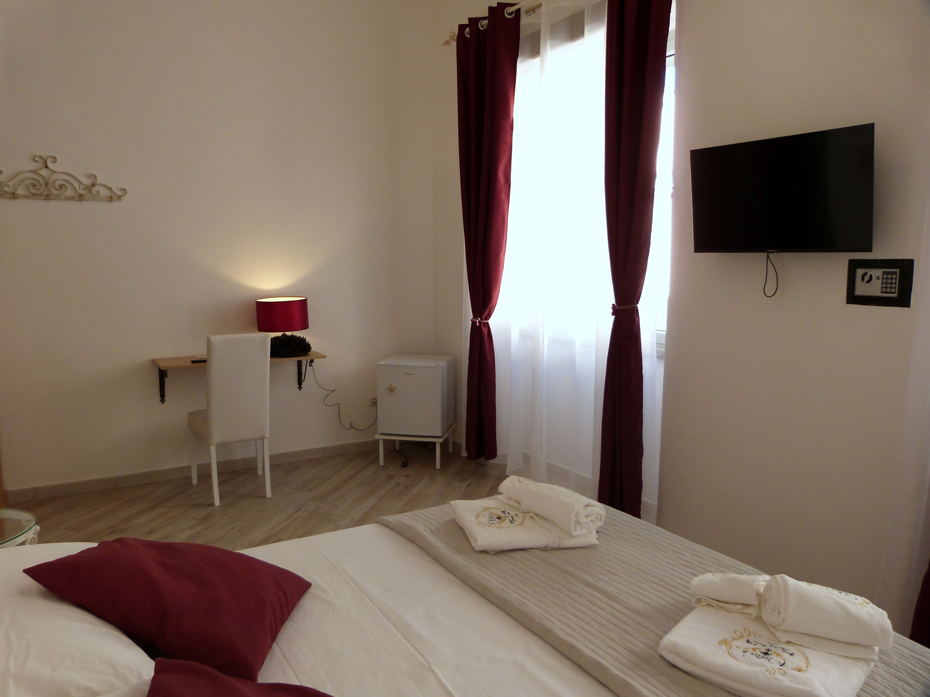 Une chambre d’hôtel avec un lit, un bureau avec une lampe, un petit réfrigérateur, une télévision et une fenêtre avec des rideaux.