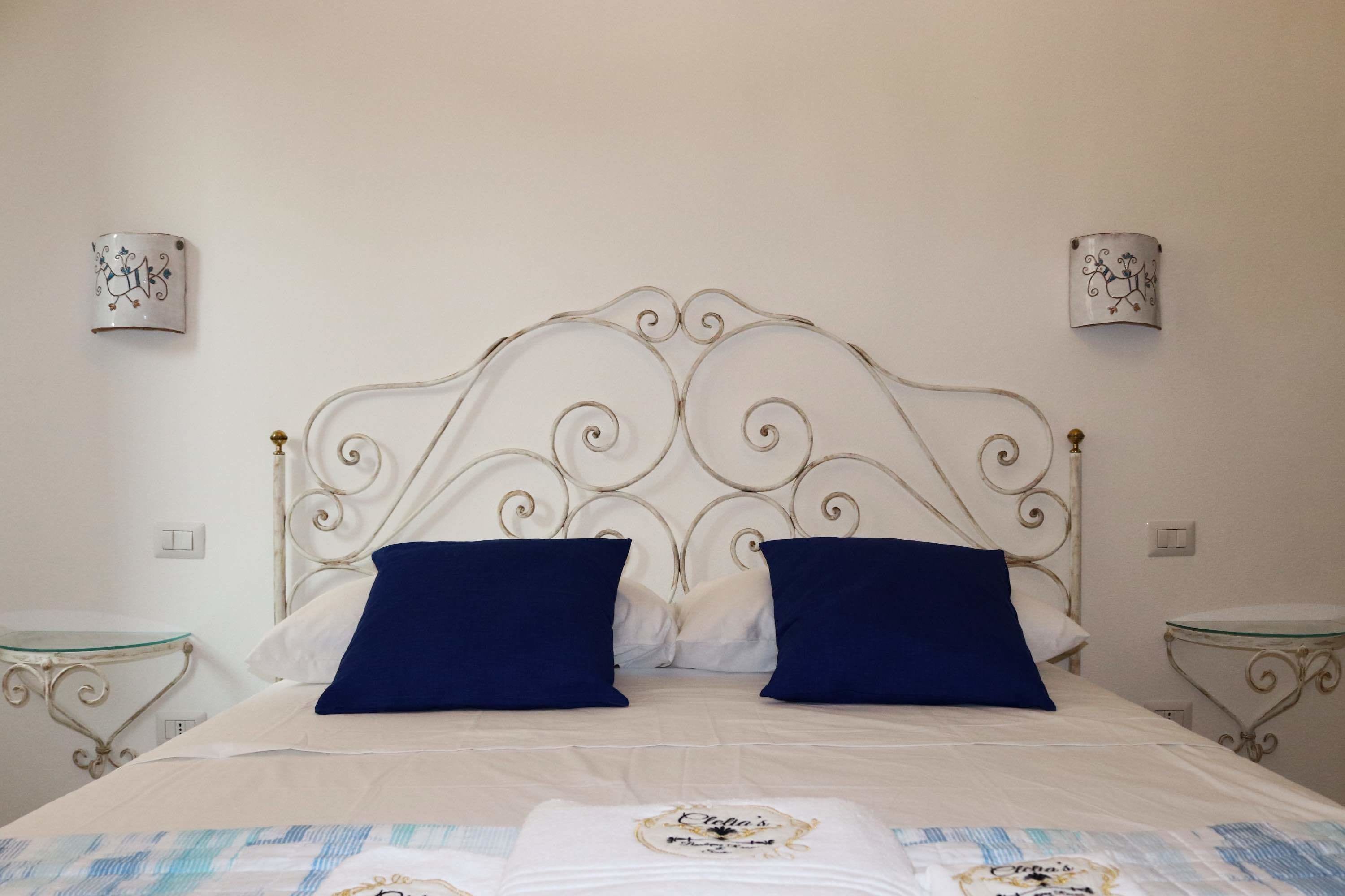 Una cama bien hecha con un tablero de cabecera decorativo, dos mesitas de noche y apliques de pared.