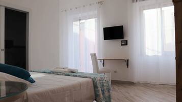Un dormitorio con cama, una silla, un escritorio, un televisor y una ventana con cortinas.