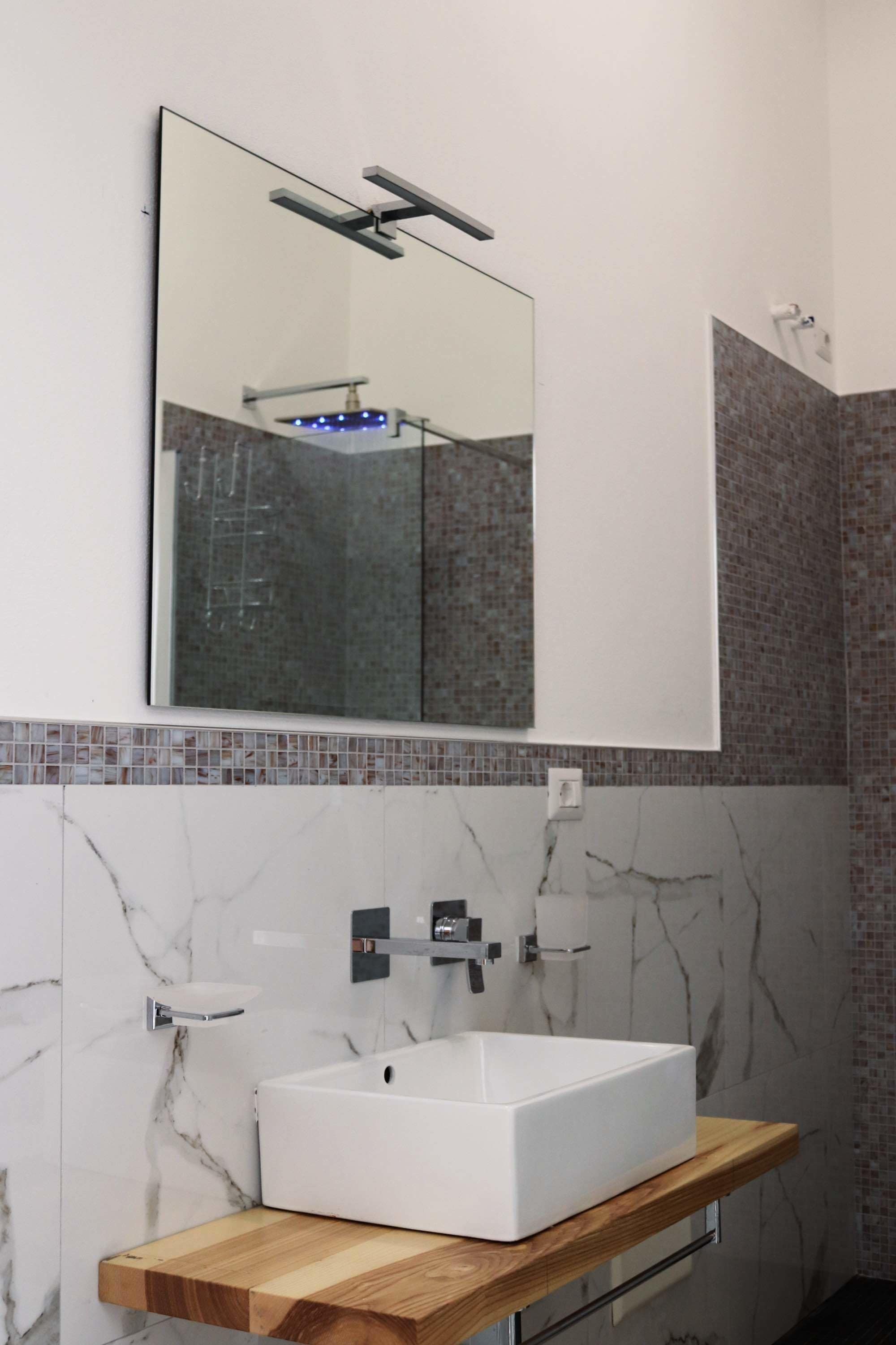 Un baño moderno con un lavamanos blanco, un espejo y una ducha.