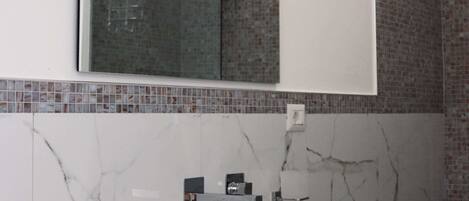 Un baño moderno con un lavamanos blanco, un espejo y una ducha.