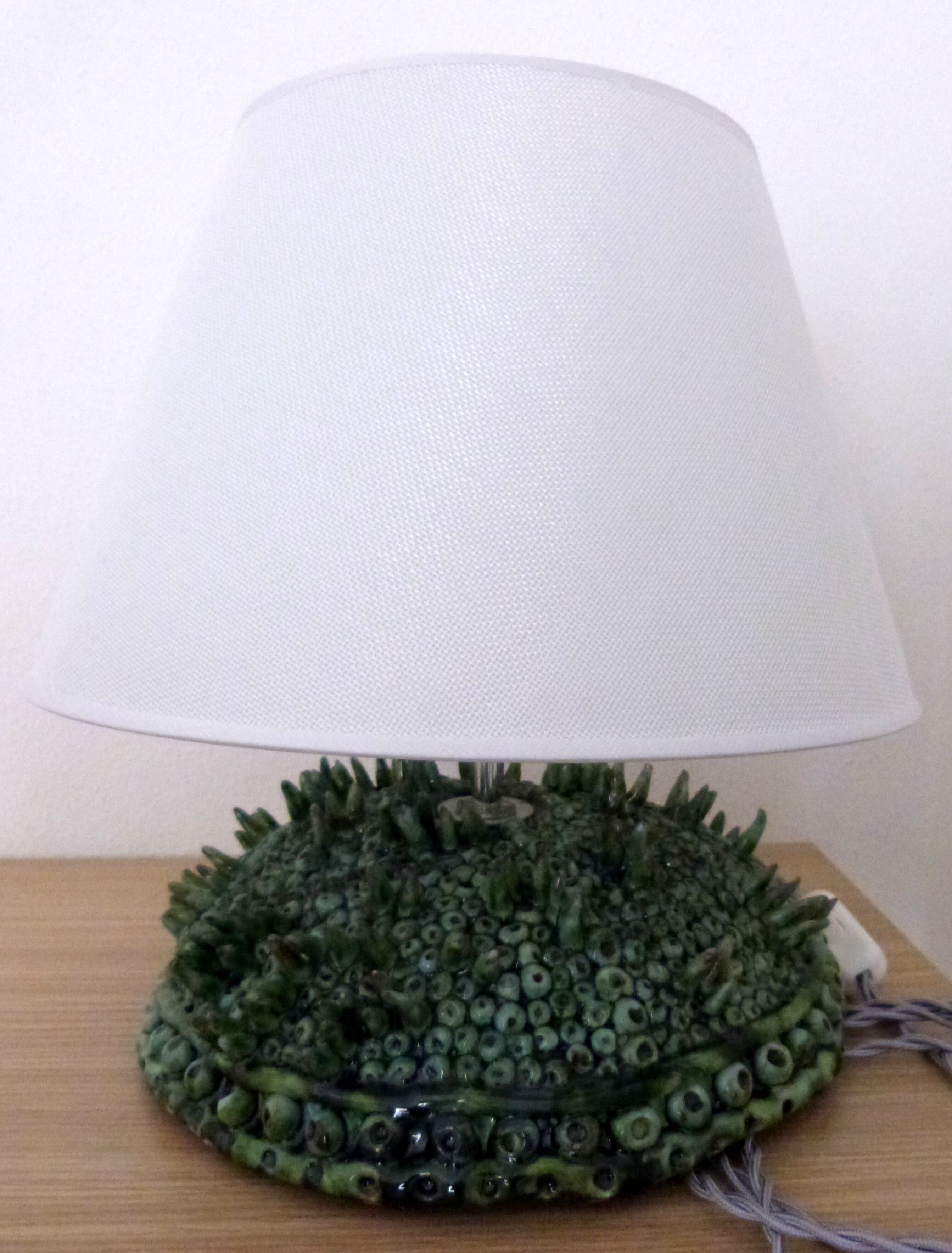 A lamp with a textured base and a white lampshade on a wooden surface.