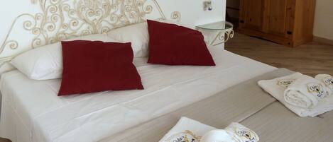 Una cama bien hecha con almohadas rojas, una obra de arte decorativa encima y un armario de madera al fondo.