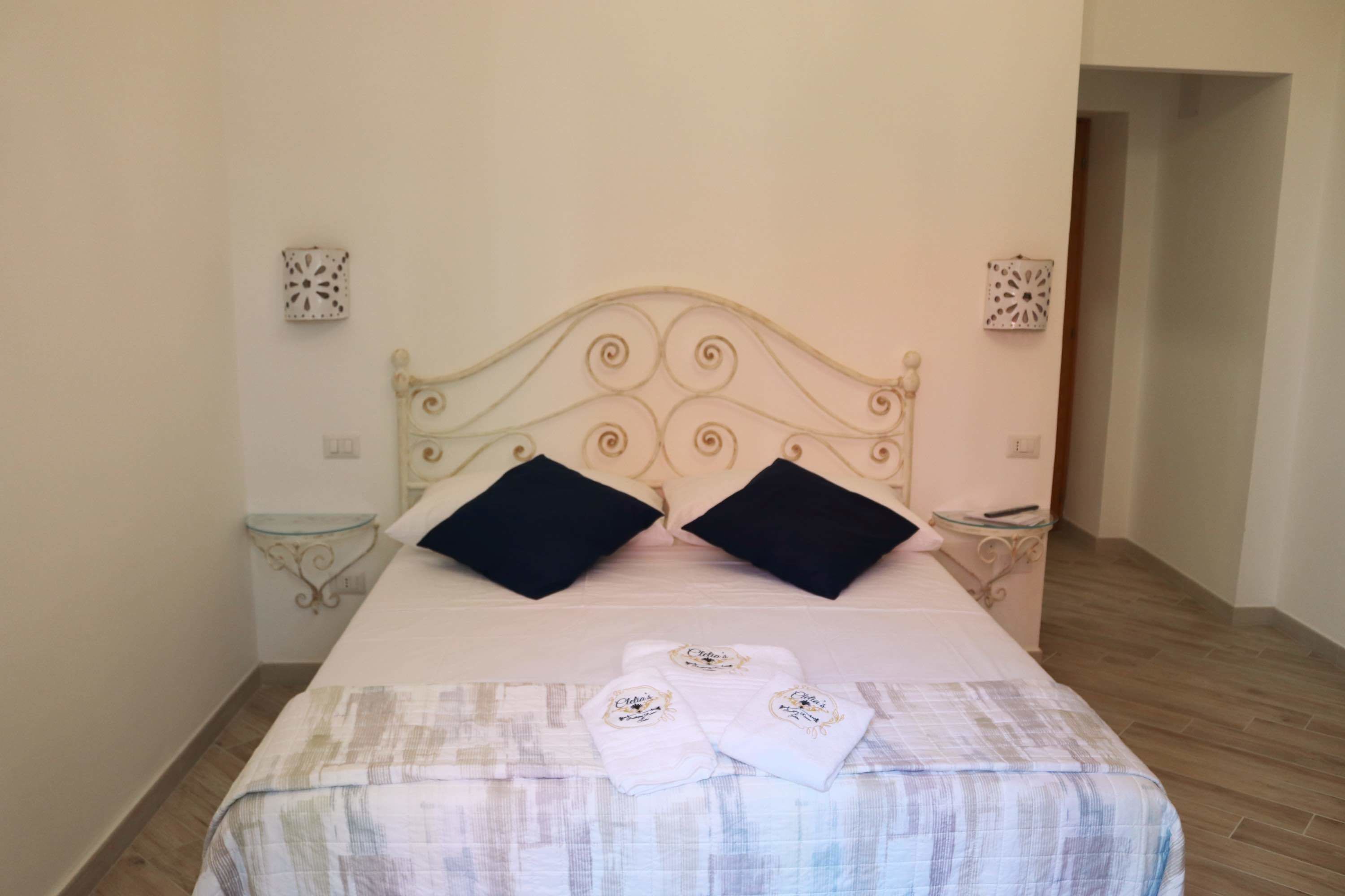 A neatly made bed with a patterned bedspread, two black pillows, and two folded towels with a logo on them.