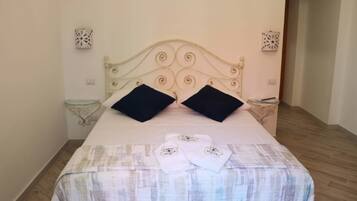 A neatly made bed with a patterned bedspread, two black pillows, and two folded towels with a logo on them.