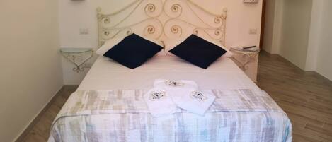 A neatly made bed with a patterned bedspread, two black pillows, and two folded towels with a logo on them.