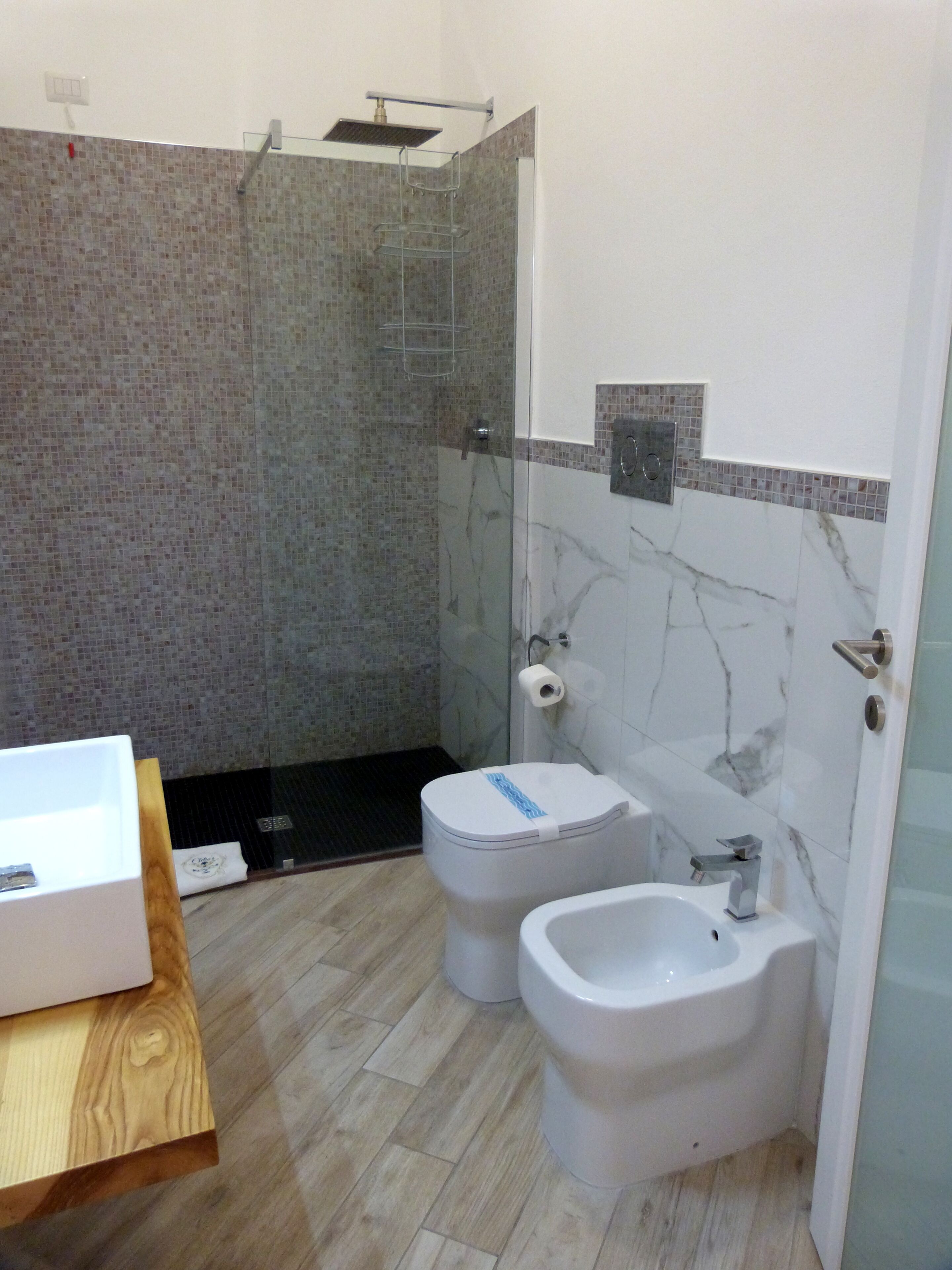 A bathroom with a shower, toilet, bidet, and a sink.